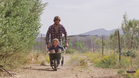 Happy-caucasian-father-and-son-pushing-wheelbarrow