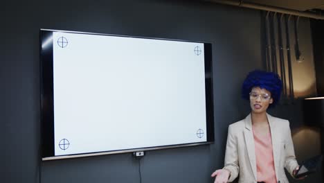 mujer de negocios casual biracial haciendo una presentación con una tableta en la oficina, espacio de copia, cámara lenta