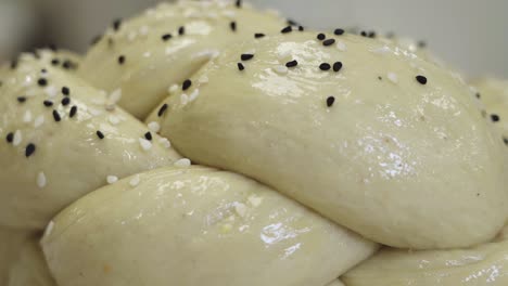 toma macro de masa de pan bellamente trenzada mientras las semillas de sésamo se rocían encima