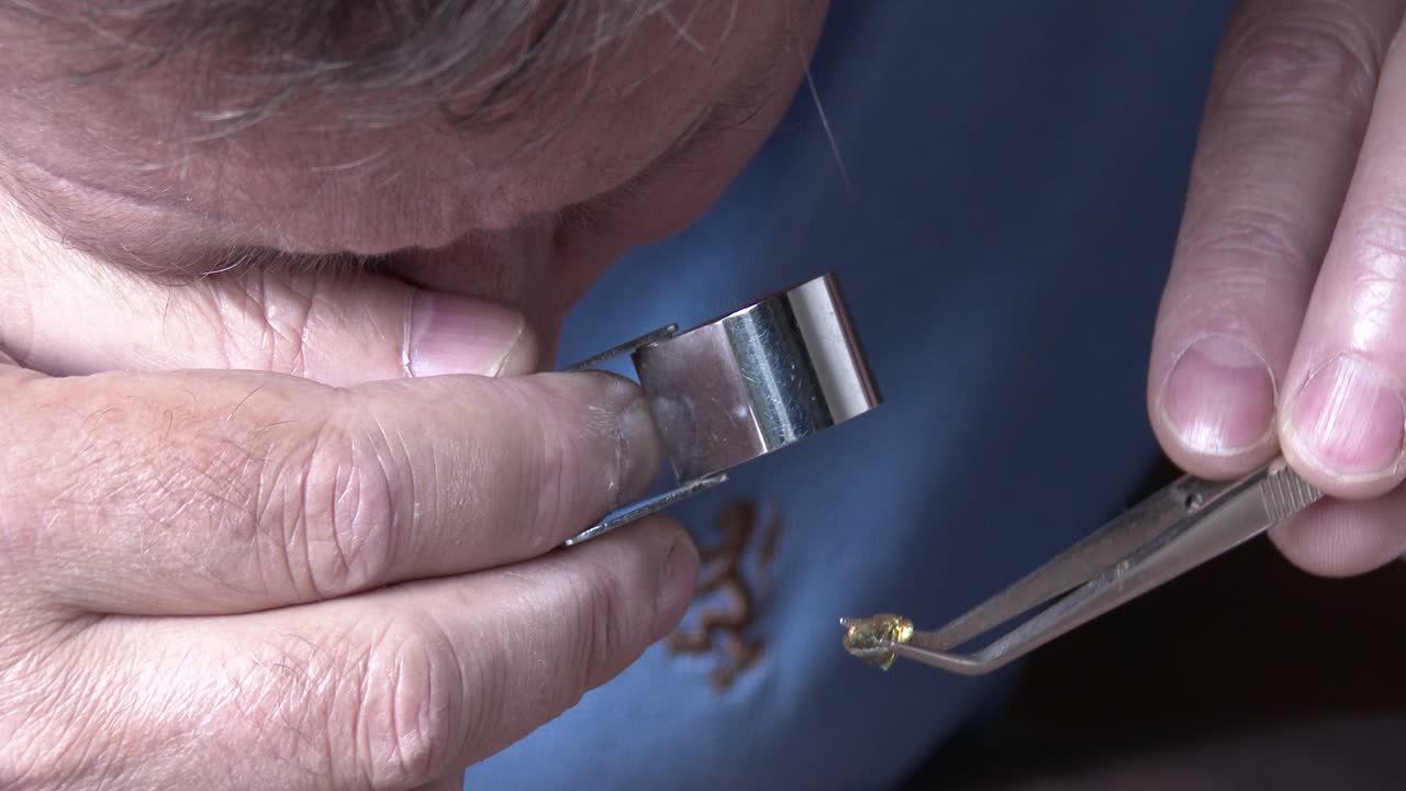 un joyero inspeccionando una piedra preciosa a través de una lupa, de cerca