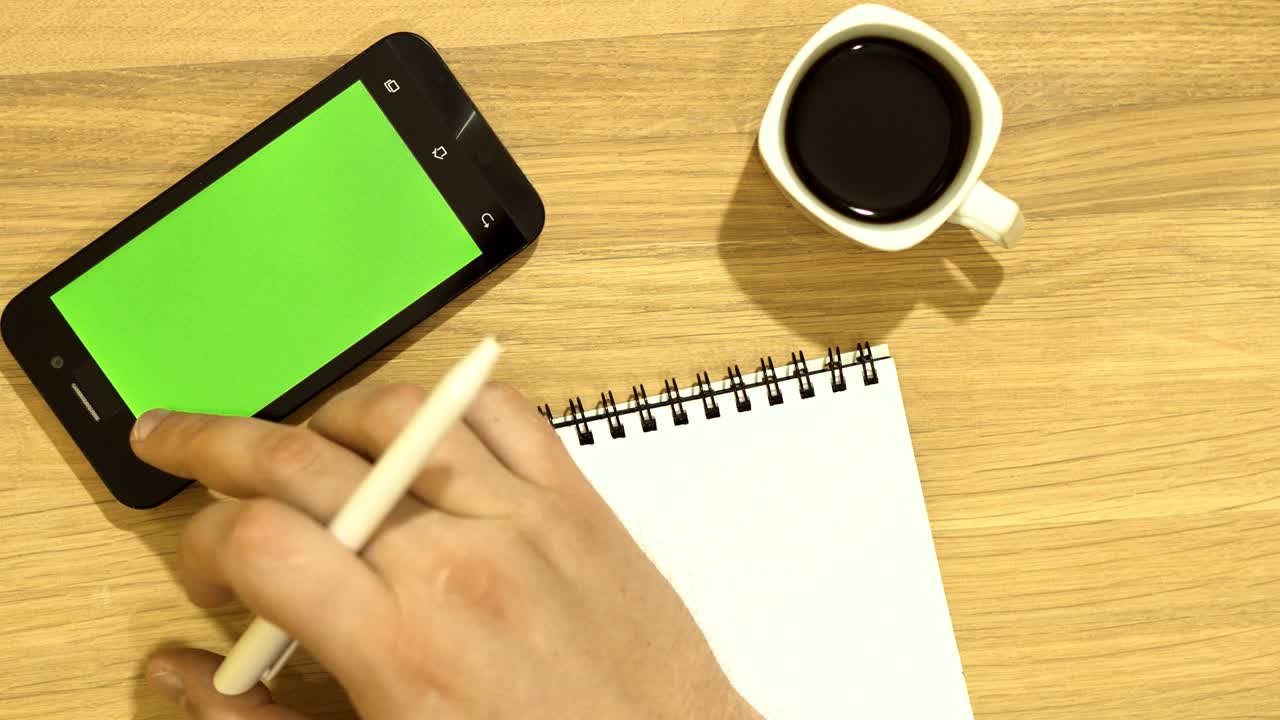 The specialist is sitting at the desk. There is a pen in his hand. Use the tablet in operation. Green screen.