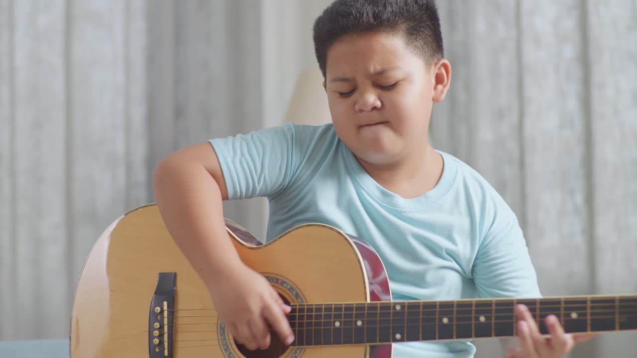 재능있는 아시아 아이의 클로즈업, 표현력 있는 얼굴, 집에서 소파에서 기타를 연주하는 것을 즐긴다.