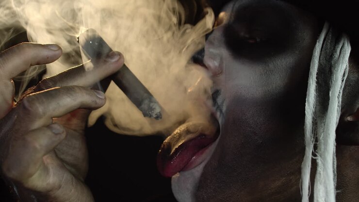 Scary guy in carnival costume of Halloween skeleton smoking cigar, making faces, showing tongue