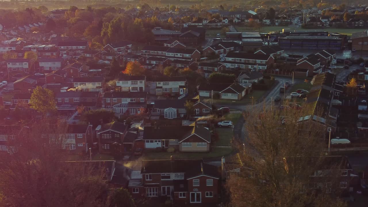 Northwest UK Townhouse estate aerial view with early morning sunrise light leaks over Autumn coloured trees and rooftops
