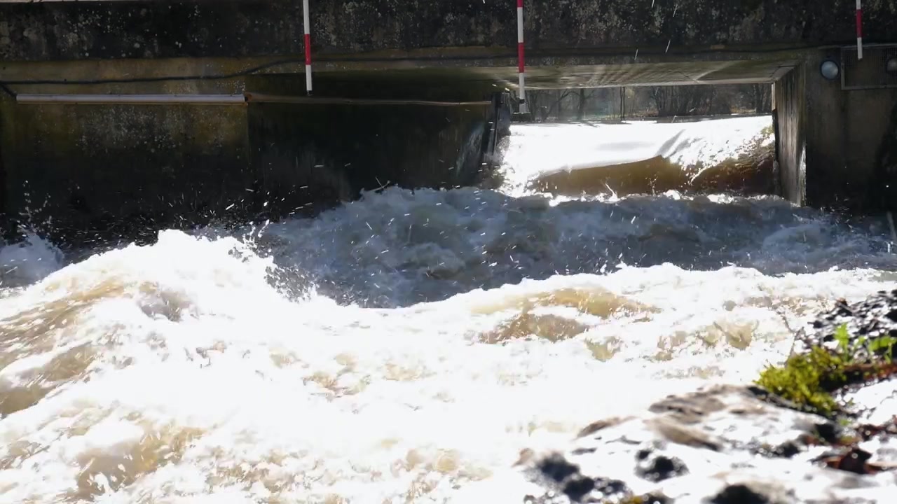 Movimento rallentato di un fiume turbolento sotto il ponte con porte a strisce sospese per i canoisti che praticano lo slalom