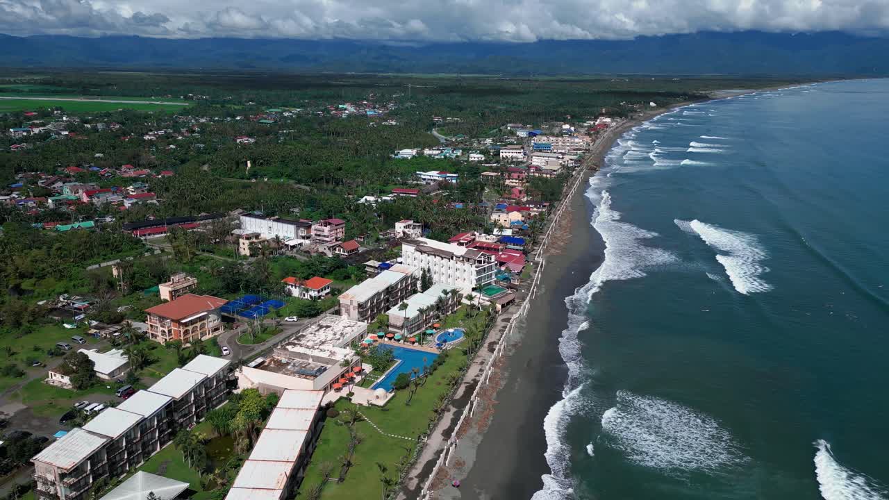 A wide drone shot captures a beautiful resort nestled along the shoreline, with the ocean's calm waves gently lapping at the sandy beach.
