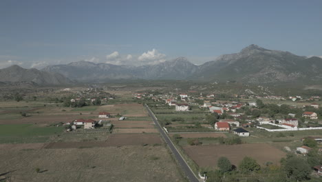 Drone-shot-flying-over-the-wide-valley-in-Albania-near-Shkoder-with-vineyards-underneath-and-mountains-in-the-background-on-a-sunny-day-with-some-clouds-LOG