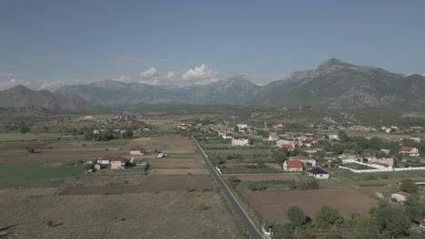 drone shot flying over the wide valley in albania near shkoder with vineyards underneath and mountains in the background on a sunny day with some clouds log