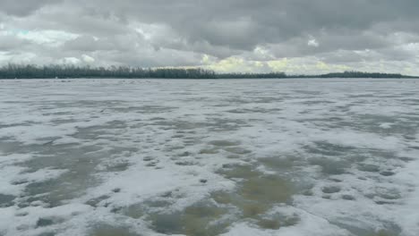 half frozen river covered with snow against dense forest