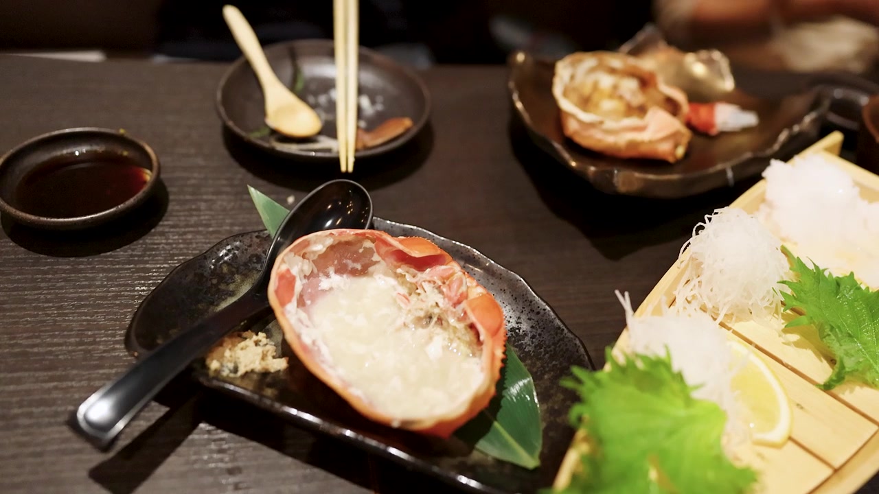 レストランのテーブルに置かれたタラバガニの味噌と刺身をハイアングルで手持ち撮影したショット。
