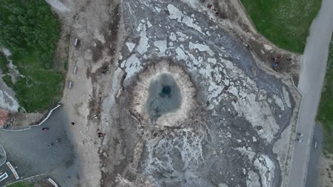 drone filmado directamente por encima del cráter de aguas termales geysir en islandia, destacando la piscina geotérmica profunda, los depósitos minerales y el terreno circundante.