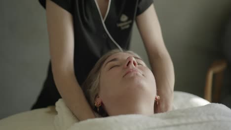 masseuse diffusing scented oils before massaging female clients shoulders on table