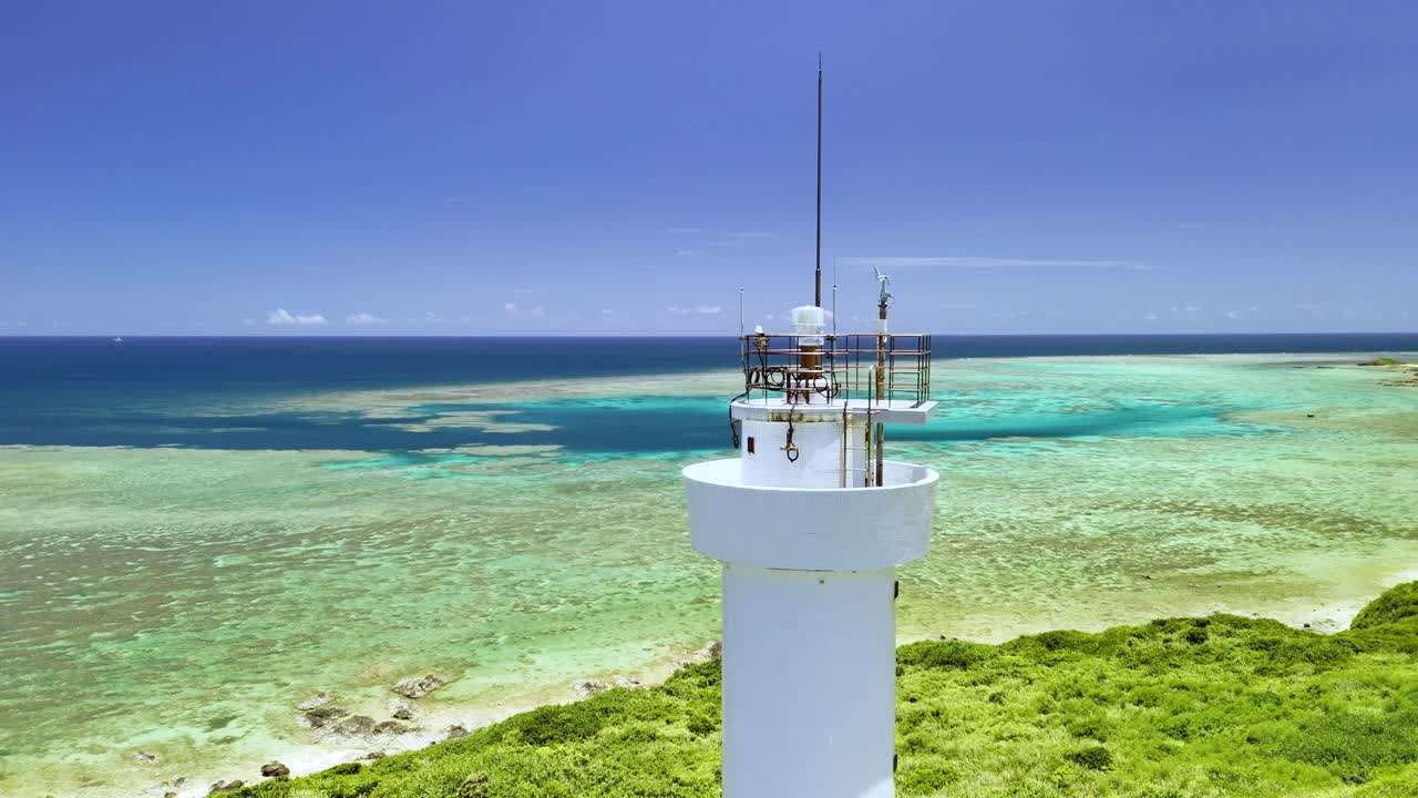 Eine detaillierte Luftaufnahme des Laternenraums des Leuchtturms Hirakubozaki, die schwenkt, um eine atemberaubende türkisfarbene Korallenriff-Lagune und den tiefblauen Pazifikhorizont in Ishigaki zu enthüllen.