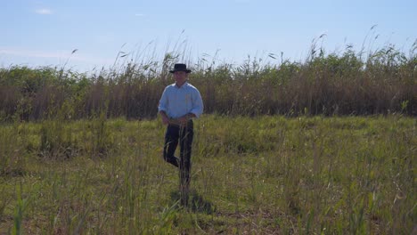 cowboy man walking in in a field with long grass in his hand