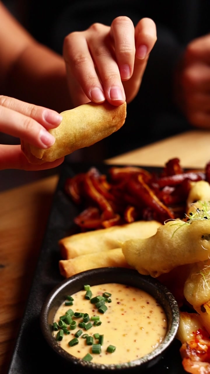 Person Picking Up a Crispy Spring Roll from a Platter