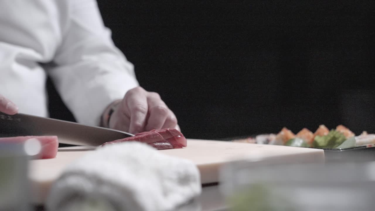 A static shot of tuna being sliced into thin pieces for sushi, showcasing precise sushi preparation. Ideal for highlighting the art of slicing fish and Japanese cuisine in food presentations.