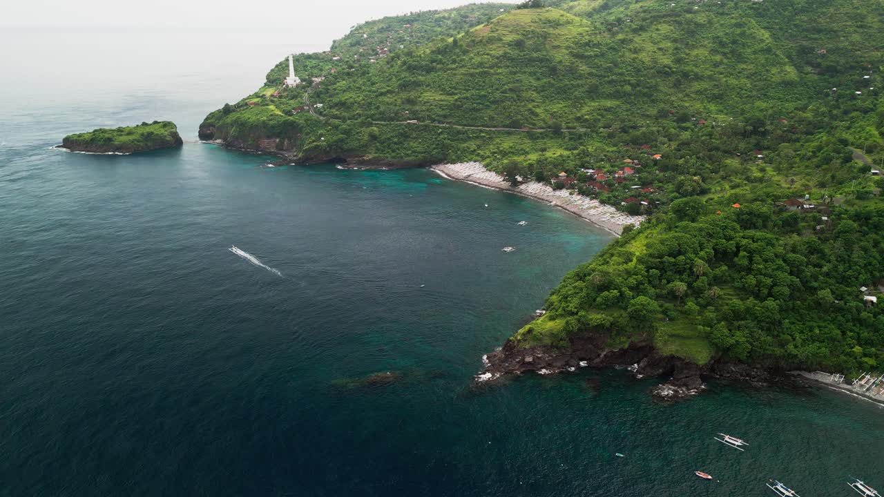 Riprese aeree con drone mostrano un villaggio di pescatori indonesiano costruito lungo una costa curva con barche tradizionali che riposano sulla spiaggia e un terreno montuoso verde che si estende nell'entroterra