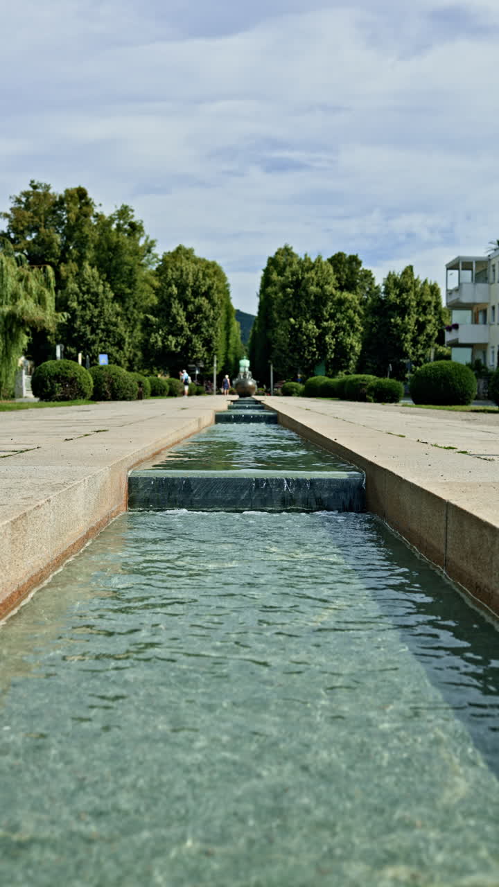 Una plaza peatonal con un río artificial en el centro. Un estanque transitable con bordes de hormigón. Un diseño arquitectónico con un río artificial en un parque urbano.