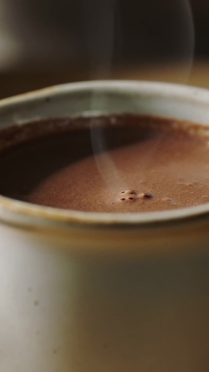 Vertical video: Beginning clip showing ceramic mug on kitchen table steaming coffee with bubbles