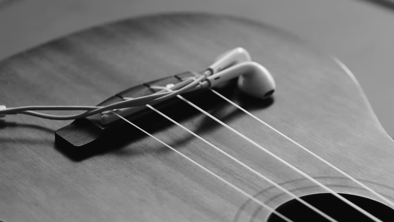 A set of earphones get placed on top of a ukulele musical instrument.