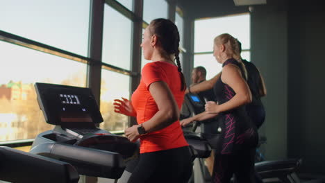 a group of people running on a treadmill in a fitness room performing a cardio workout. men and women train together running indoors warm-up before training in slow motion.