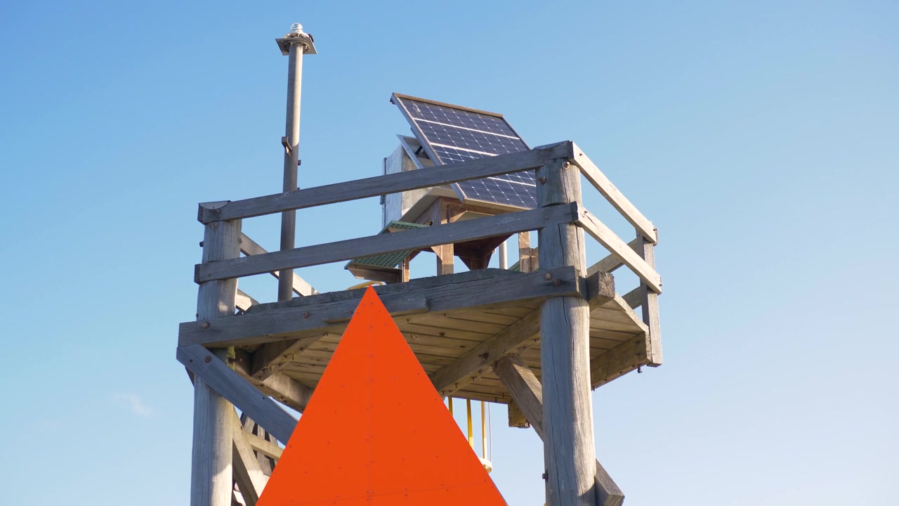 Slow motion landscape of a signal beacon monitor observation platform with an antenna orange marker sign and a solar panel mounted on a wooden framework in Port of Newcastle Australia maritime tourism