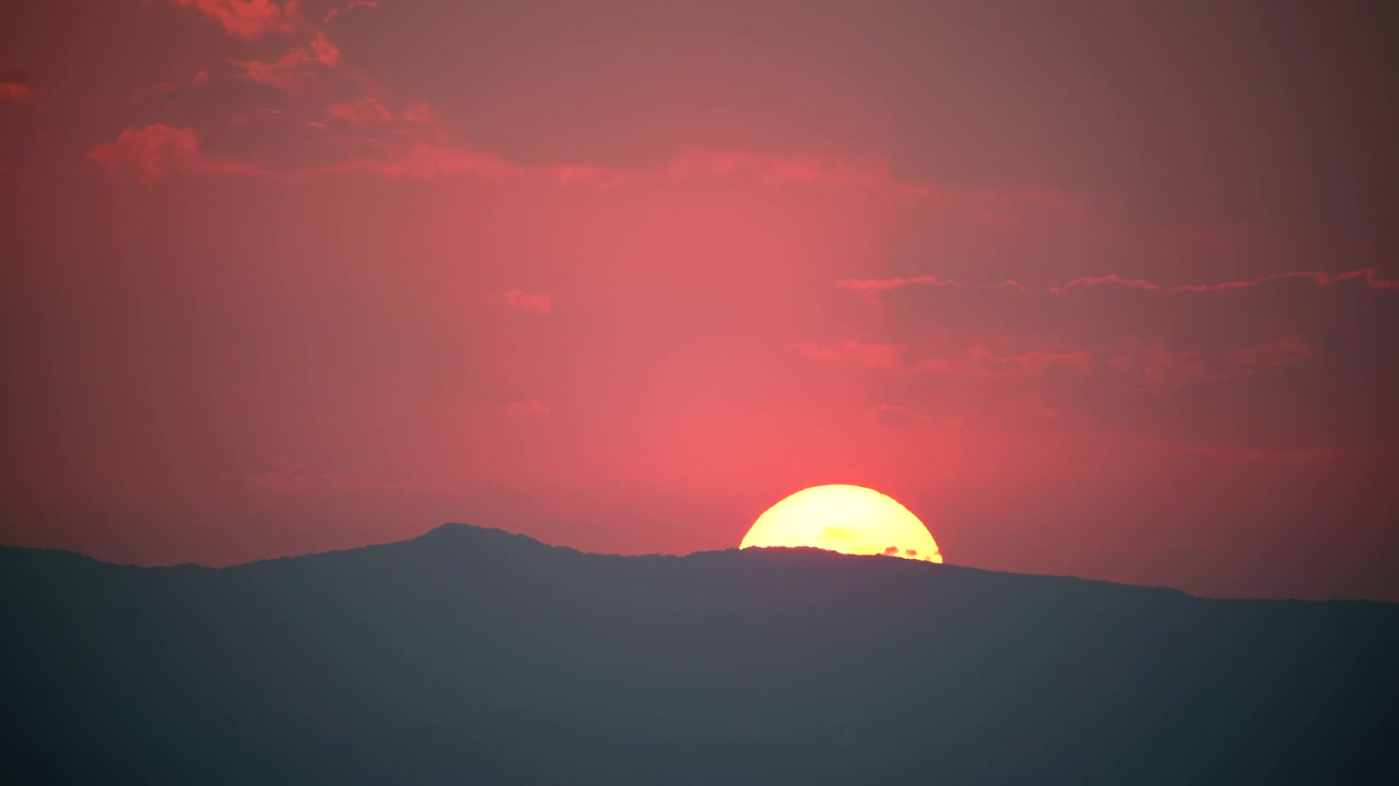 Matahari Terbenam di Balik Siluet Gunung saat Senja