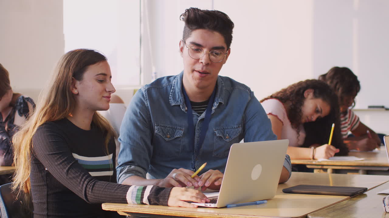 profesor masculino dando apoyo uno a uno a una estudiante que trabaja en el escritorio en la computadora portátil