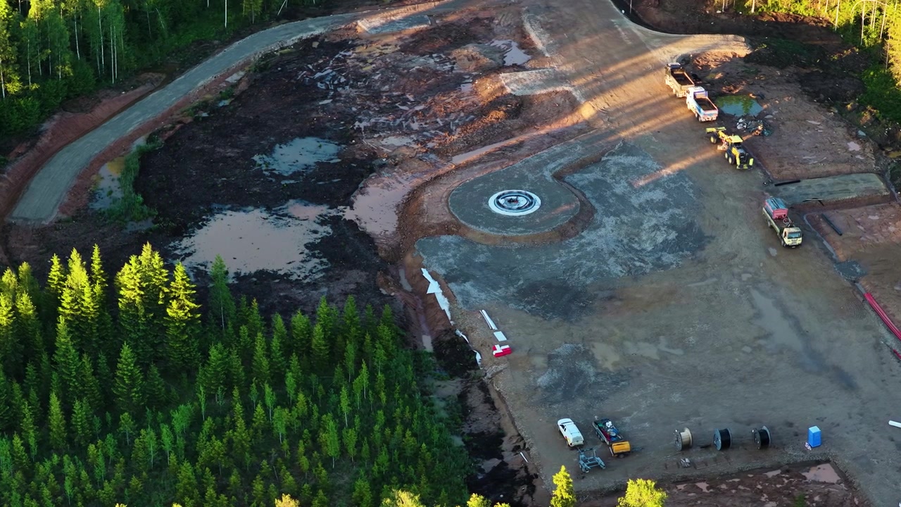 Aerial view of a wind turbine foundation construction site next to a lush green forest
