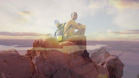 Composite-of-happy-hiking-african-american-woman-sitting-on-rock,-and-setting-sun-over-lake