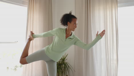 woman practicing yoga at home, balancing gracefully in dancer pose near window
