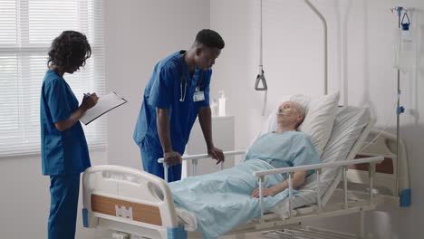 senior patient on bed talking to 2 african american doctor in hospital room health care and insurance concept. doctor comforting elderly patient in hospital bed or counsel diagnosis health.