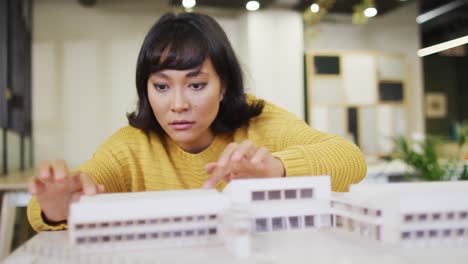 biracial businesswoman sitting at table and working with model at office