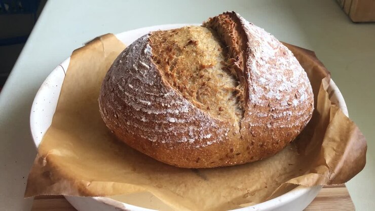 Baker puts freshly baked sourdough bread on wooden board.
