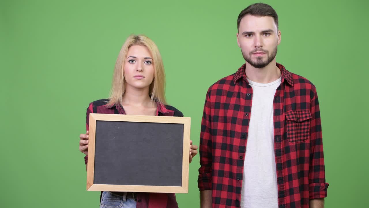 Young couple holding blackboard and pointing finger together