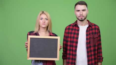 young couple holding blackboard and pointing finger together