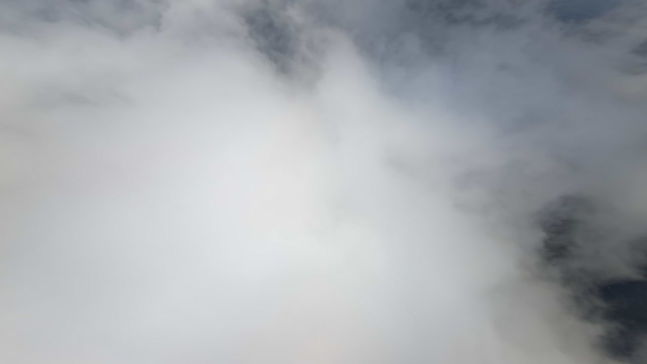 Thick white clouds in the sky. Footage from FPV drone flying through the cloudscape and revealing view on the land below.