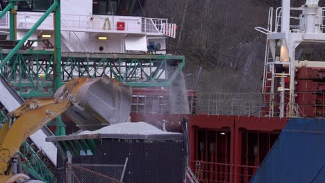 dumper truck emptying his bucket of anorthosite minerals for loading into ships bulk cargo hold - dumper in front with conveyor belt in middle and ship in background - gudvangen norway static