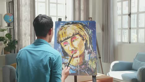 Hind View Of An Asian Artist Man Holding Paintbrush Mixed Colour And Thinking Before Painting A Girl'S Hair On The Canvas