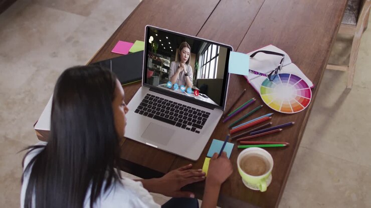 Caucasian woman using laptop on video call with female colleague, making notes