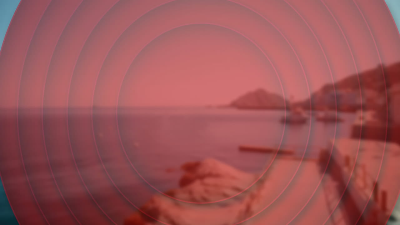 Red concentric circles animation over serene coastal landscape with rocky shoreline