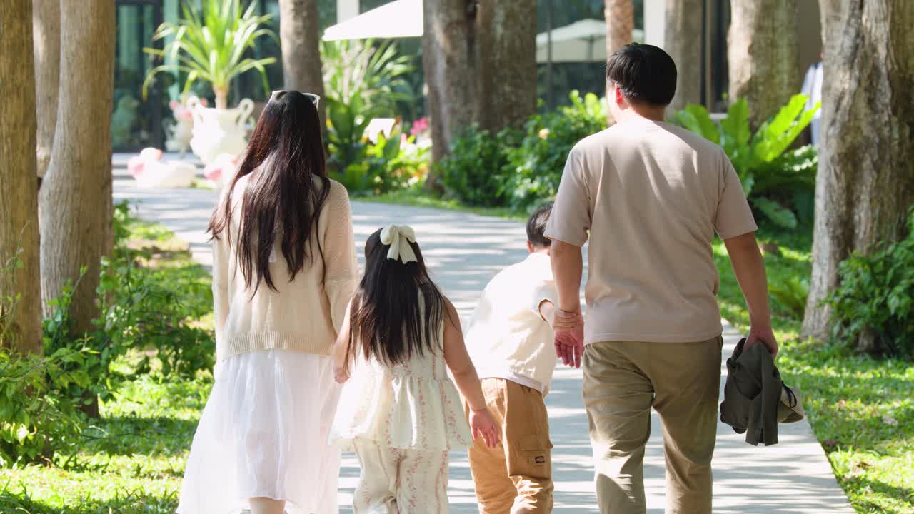 Rear view of parents and children walking along a sunlit garden path during daytime