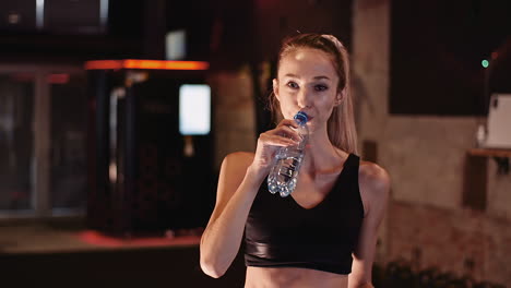 young female athlete drinking water from bottle after workout session at health club 3