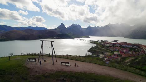 Static-aerial-shot-with-parents-swinging-their-child-on-the-swing-at-the-viewpoint-in-Riaño,-a-village-in-León,-Spain-on-the-shore-of-a-large-reservoir-in-the-Cantabrian-mountains