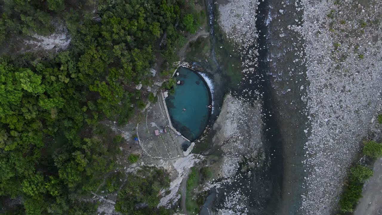 Drönarvy rakt ner mot det turkosa vattnet i Benjas termiska pool i Permet, Albanien