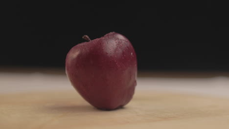 manzana fresca en una mesa girando a su alrededor con luz cálida y fondo negro en un ambiente oscuro interior con accesorios simples dispuestos uno al lado del otro