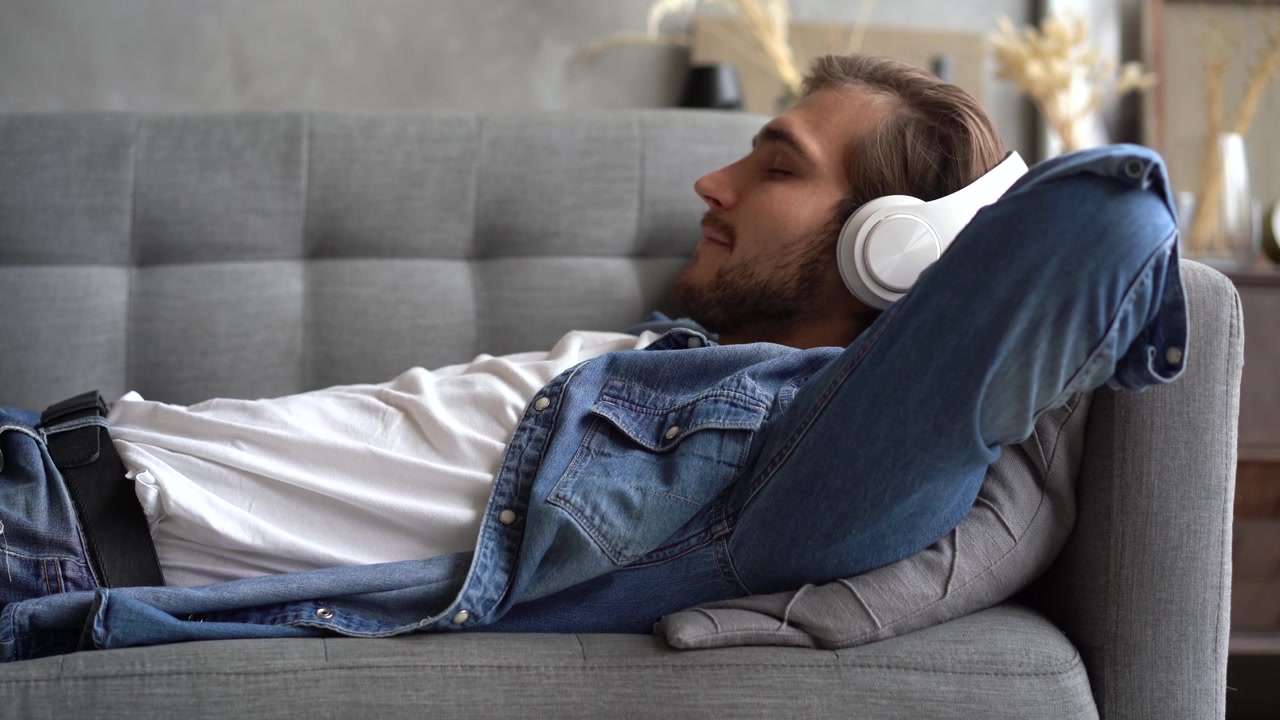 Giovane uomo rilassato sul divano mentre ascolta musica con le cuffie