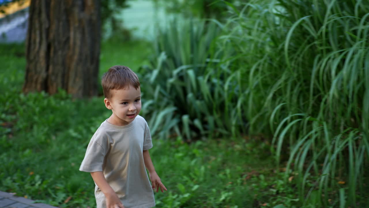Lovely boy tossing a little blue ball up. Kid runs to pick up a ball but changes his mind. Summer time fun.
