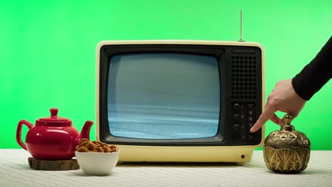 nahaufnahme eines alten retro-fernsehers auf grünem hintergrund, knöpfe drücken. gebrochener fernseher mit grauem interferenzbildschirm und antenne, roter teekannen auf dem tisch, schlechter signalempfang, kinematografie-konzept