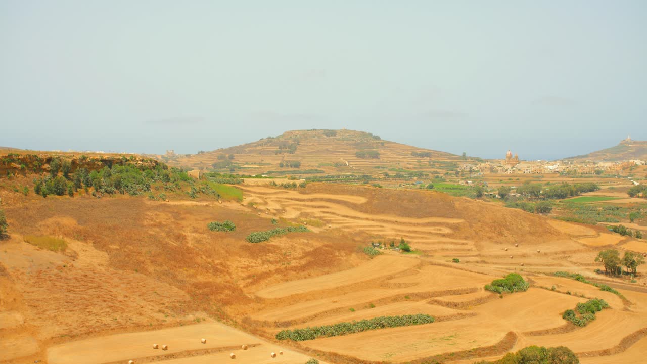 Panoramica del paesaggio dell'Isola di Gozo, vasto deserto sabbioso con piccole colline e campi.